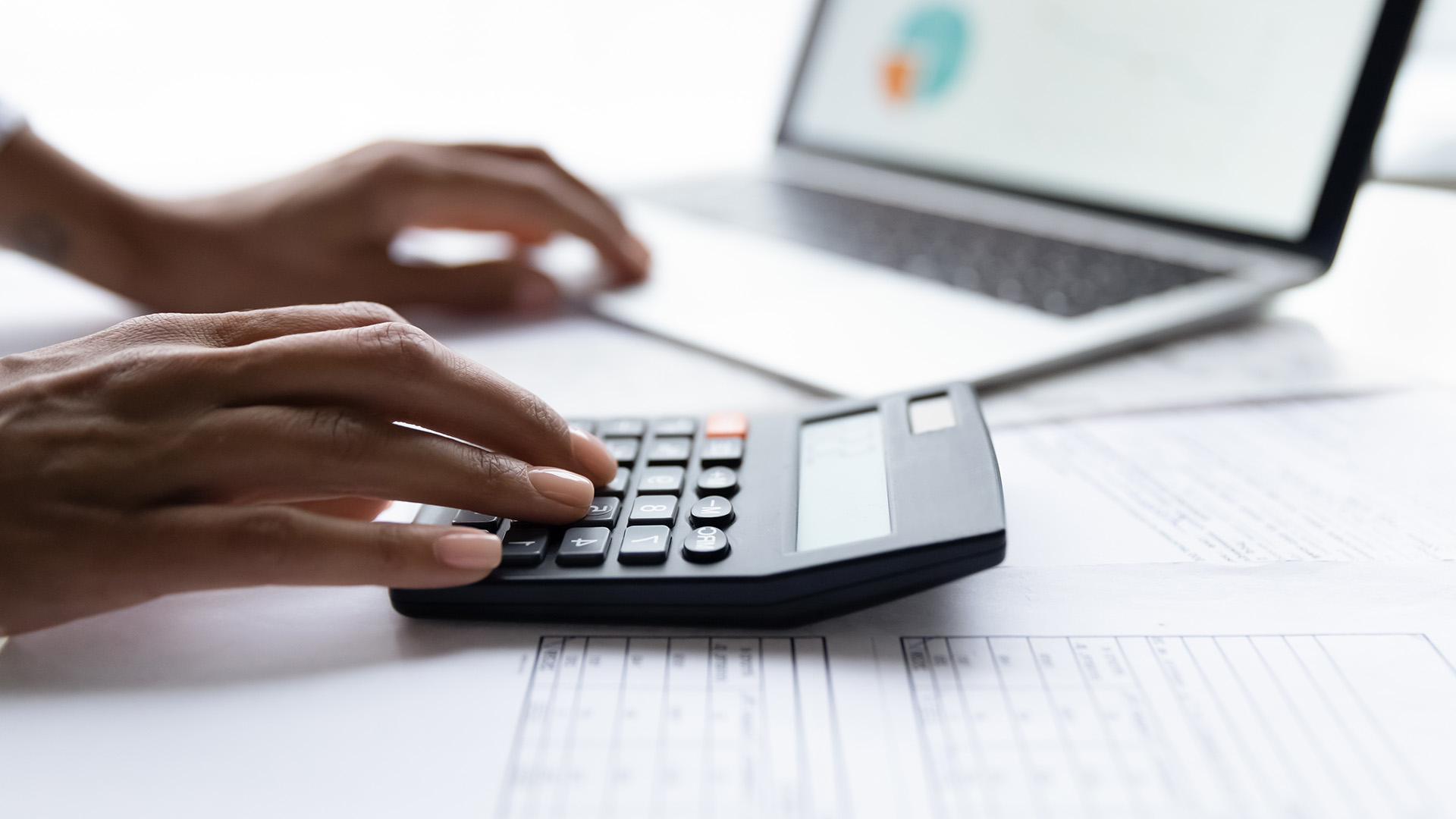 Close-up of hands using a calculator and laptop, symbolizing COI tracking software costs and 2025 pricing analysis.
