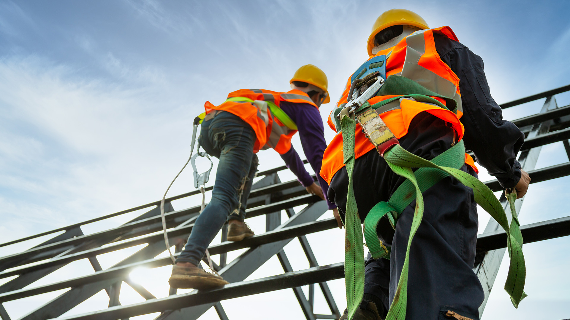 Construction workers in safety harnesses climbing a steel structure, representing jobsite risk management and COI tracking.