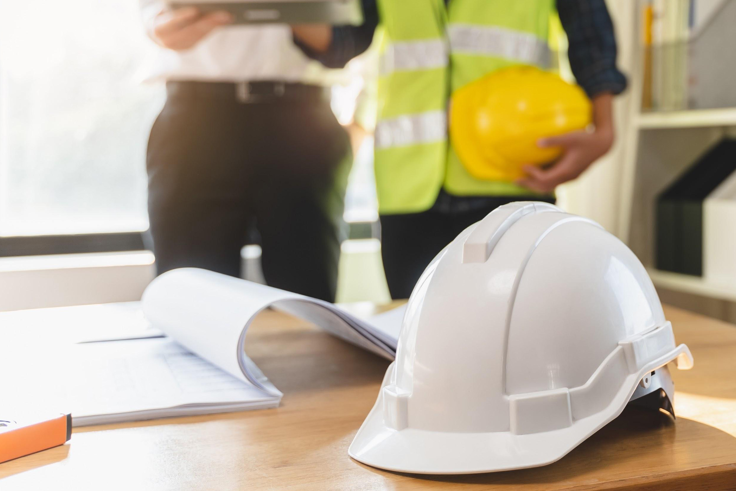 Construction site with hard hat and documents representing certificate of insurance verification for contractors.